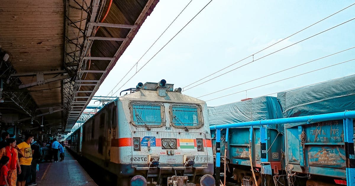 Indian railway train arriving at a busy station platform with waiting passengers